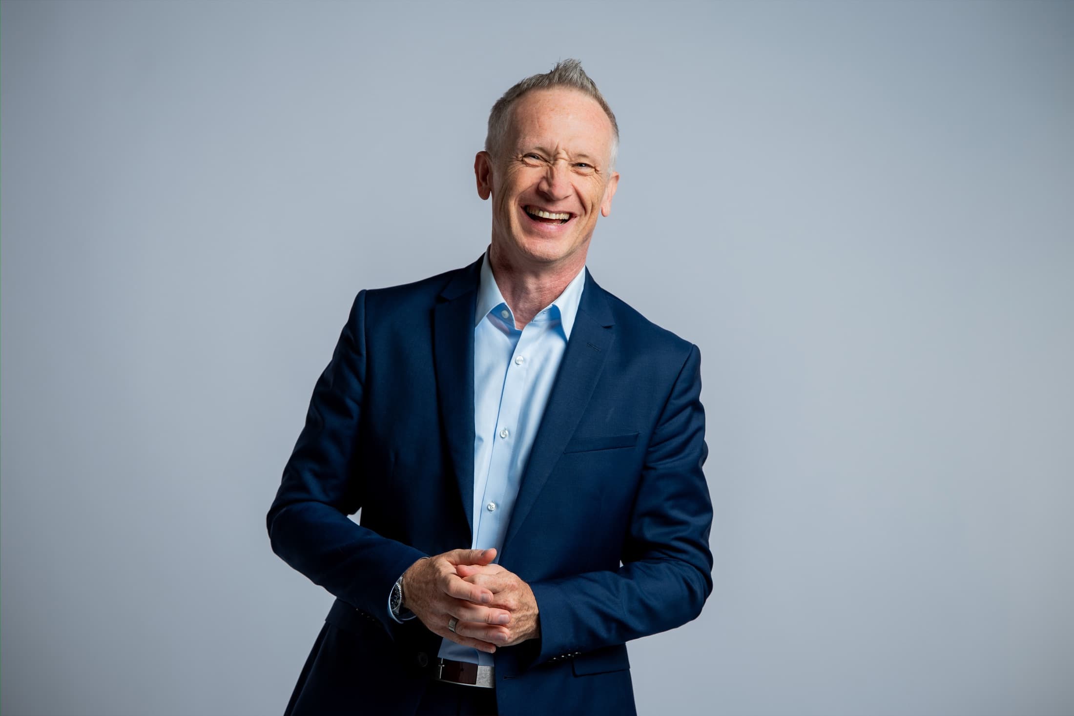 Jürgen Kob lachend im blauen Anzug vor hellem Hintergrund